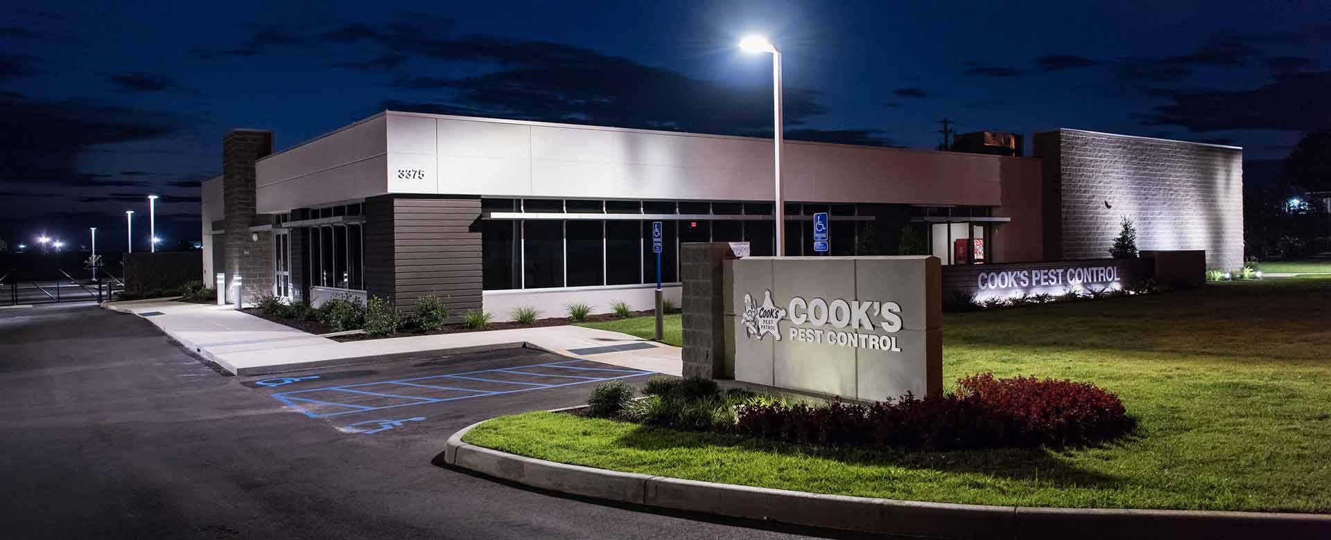 A modern commercial building at dusk with lit signage for 'COOK'S PEST CONTROL' and a landscaped front area reflecting the company's branding