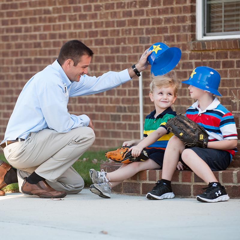 A Cook's pest control professional playfully interacts with two young children wearing toy helmets.