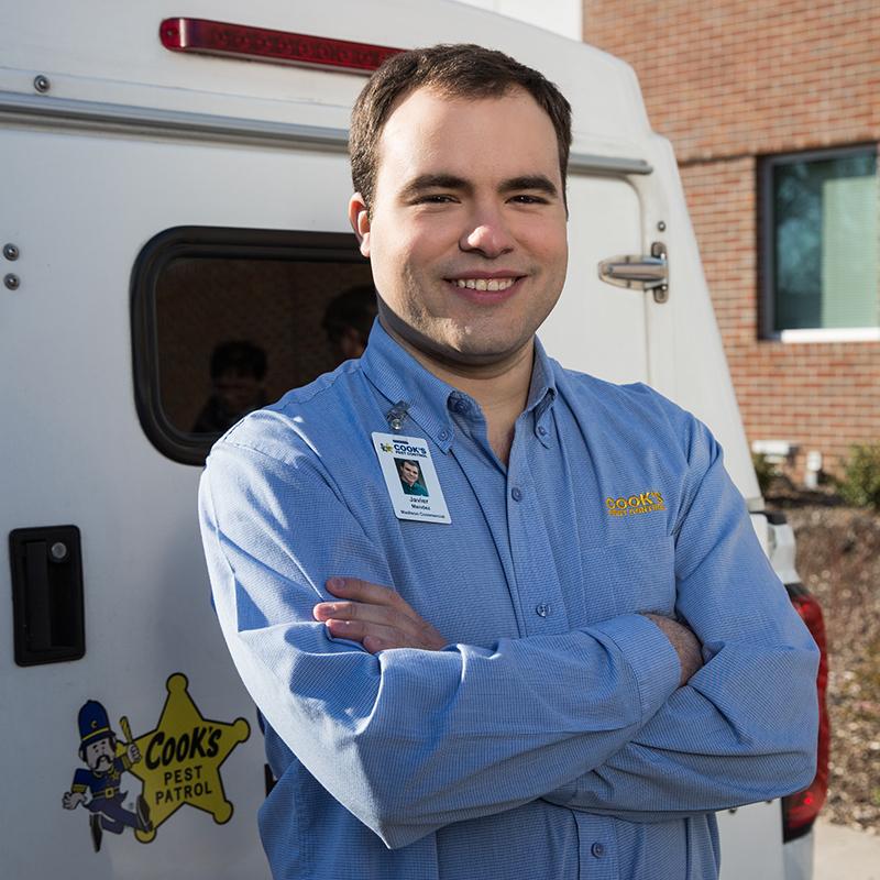 Smiling Cook's pest control technician with crossed arms standing in front of a service van.