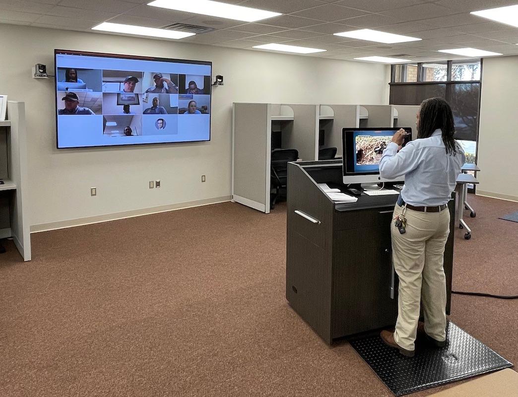 A Cook's Pest Control employee presenting in front of a video conference screen in an office.