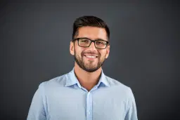 headshot of Cheerful man with glasses and a blue shirt on a gray background.