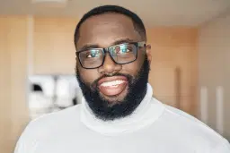 headshot of Smiling bearded man with glasses in a white sweater indoors.