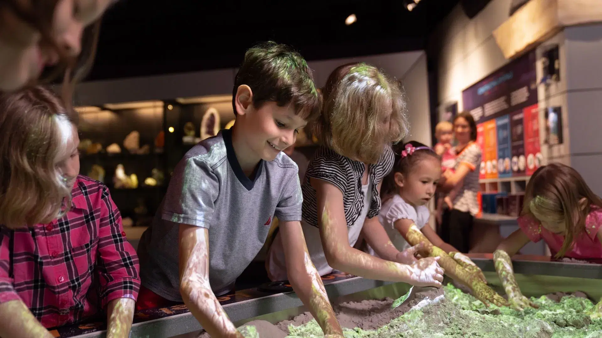 Children engaged in hands-on learning activity with kinetic sand at a museum exhibit.