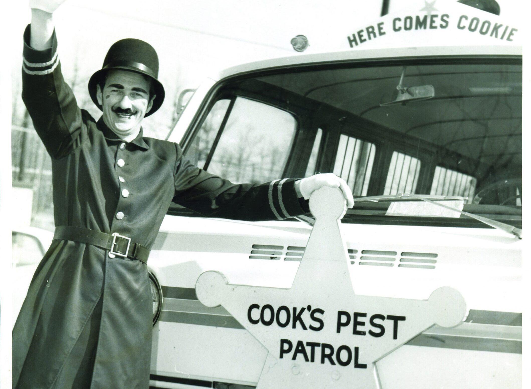 Vintage photo of a man in a top hat and uniform waving beside a Cook's Pest Patrol vehicle.